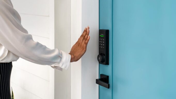 A person holds their palm in front of a Philips smart lock on a blue door.