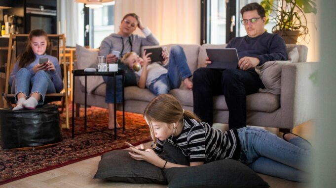 A family sits together while everyone uses a different smart device
